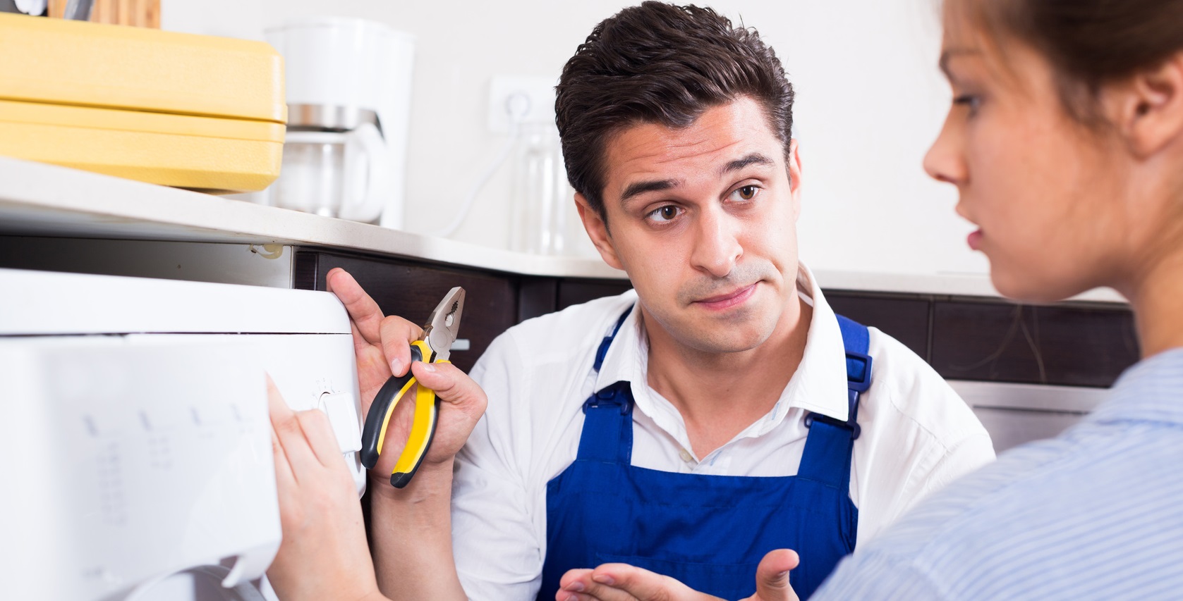 Serious serviceman and stressed woman near washing machine in kitchen